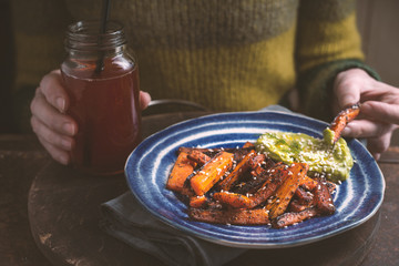 Woman eating roasted carrots with avocado sauce