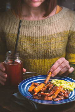 Woman in a green sweater eating fried carrot from a plate