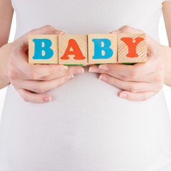 Pregnant woman holding alphabet wooden blocks. Baby sign