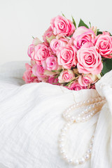 Female white dress and jewellery with fresh roses bouquet on chair