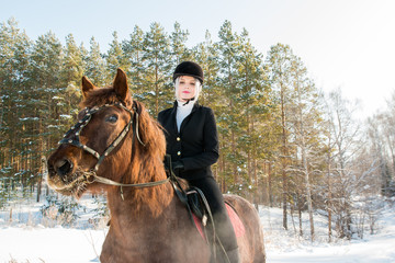 Young beautiful girl jockey riding a horse in winter forest