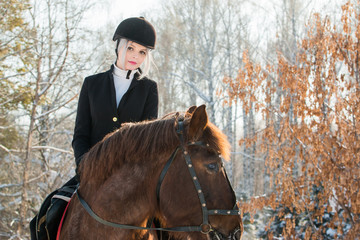 Young beautiful girl jockey riding a horse in winter forest