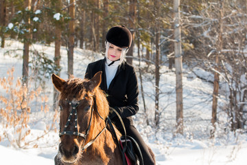 Young beautiful girl jockey riding a horse in winter forest