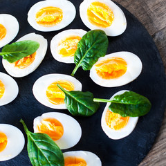 Fresh green spinach baby leaves and boiled eggs cut in a half on wooden background