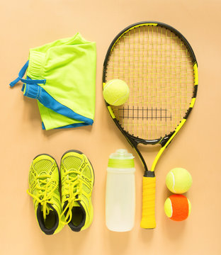 Tennis stuff on cream background. Sport, fitness, tennis, healthy lifestyle, sport stuff. Tennis racket, lime trainers, tennis ball, lime athletic shorts, sports bottle. Flat lay, top view.