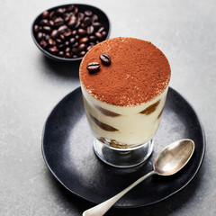 Tiramisu, traditional Italian dessert in glass on a grey stone background. Copy space