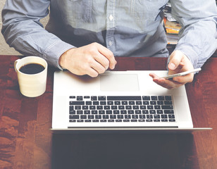 Business concept image. Man doing work with a computer. Coffee cup and phone on the table. Image has vintage effect.