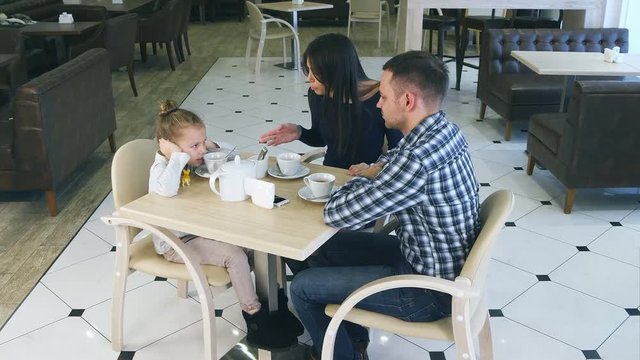 Indignant mother blaming on daughter and husband in cafe. Littke girl closing her ears.