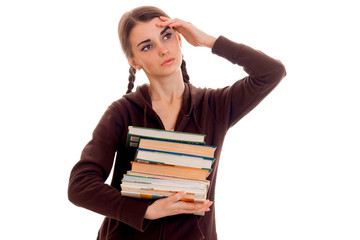 tired student girl in brown sport clothes with a lot of books in her one hand and second on her head posing isolated on white background