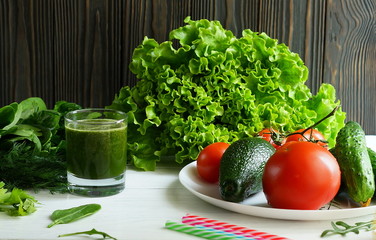 Green smoothies avocado cucumber and fresh herbs on a white wooden background.