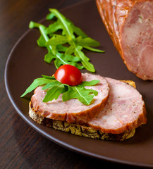 Smoked sausage, ham with red tomatoes and lamb's lettuce on a dark brown plate