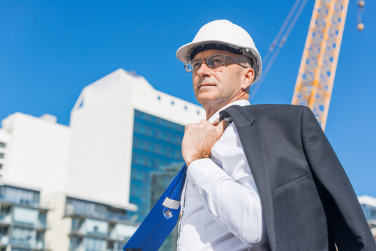Senior elegant builder man in suit at construction site on sunny summer day