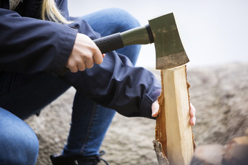 Woman Cutting Wood For Bonfire On Campsite