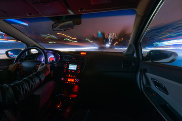 hands on the wheel a car moves at fast speed at the night. Blured road with lights with car on high speed. Car speed night drive on the road in city
