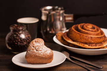 a cake with sugar powder on a plate, a cinnamon roll and coffee in a jar