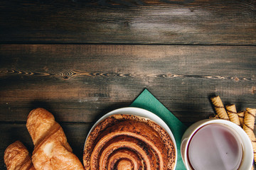 bun with cinnamon, chocolate sticks, croissants and a cup with a drink