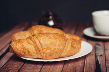 two croissants in a plate and a cup with a drink in the background
