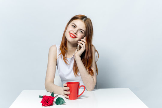 happy woman with phone sitting at table, red mug and flower - Powered by Adobe