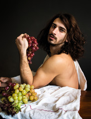 photo beautiful half naked curly guy at the table with a bunch of red grapes