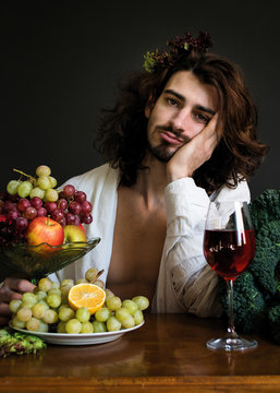 photo half naked curly guy at a table with fruits and wine bored