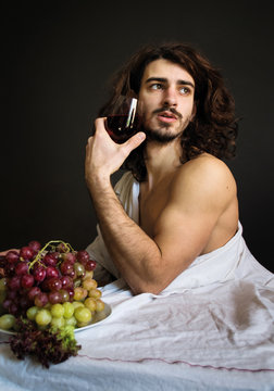photo half naked curly guy at the table with a plate of grapes and a glass of drink
