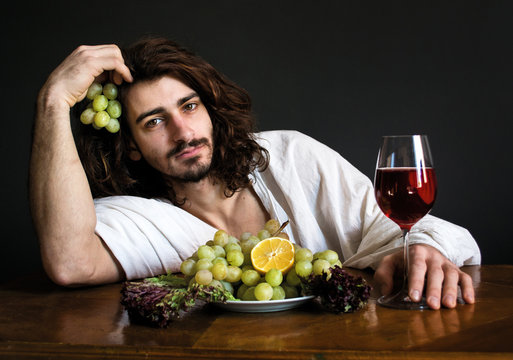 photo half naked curly guy at the table with a plate of grapes and a glass of wine