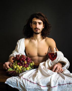 photo half naked curly guy sitting at a table with fruits and wine