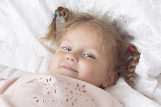 Little girl has fun in a bed. Portrait of child in the bedroom.