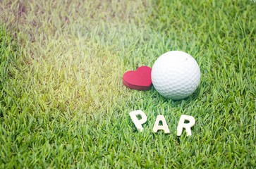 Golf ball and red heart on green background.
