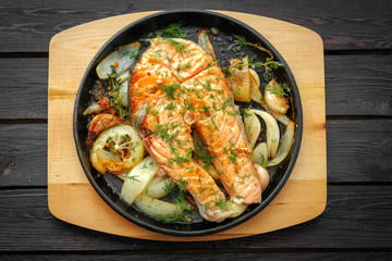 Frying pan with salmon steak, stir-fry veggies, lemon, onion and herbs.