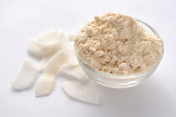 Coconut flour and flakes on white background. Cream powder in a glass bowl. Isolated on white. Alternative gluten-free flour for baking and cooking
