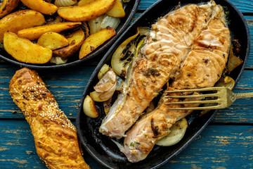 Frying pan with salmon steak, stir-fry veggies, lemon, onion and herbs.