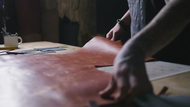 Craftsman work with big peace of leather at workshop, slow motion, close up