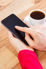 Hand of woman touching blank screen of mobile phone, cup of coffee