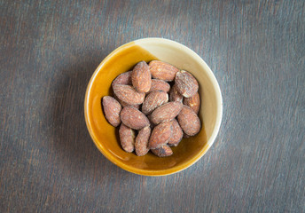 Almonds in brown bowl on wooden background.