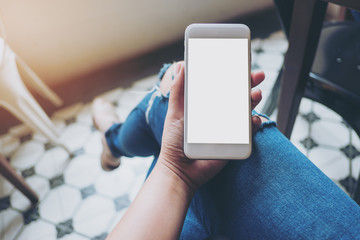 Mockup image of hand holding white mobile phone with blank white screen on thigh with a vintage tile floor in cafe , feeling relax