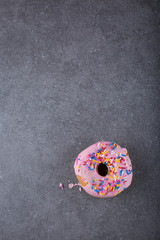 A frosted donut/doughnut with sprinkles. Gray background