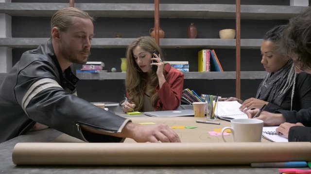 A millennial professional woman talking on the phone with her coworkers working