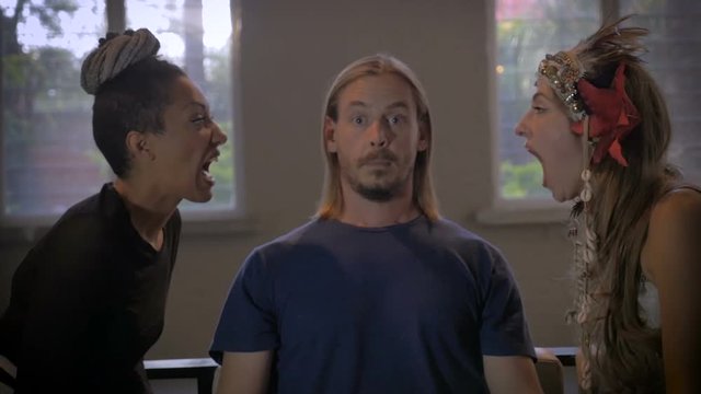 Two beautiful women scream at a millennial man while his eyes open wide