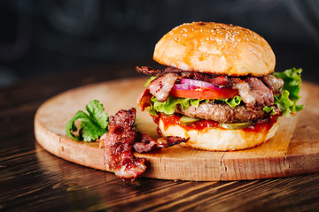 Burger with bacon, meat, tomato and lettuce   on wooden background. Close up