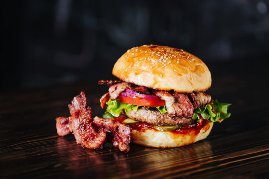 Burger with bacon, meat, tomato and lettuce   on wooden background. Close up
