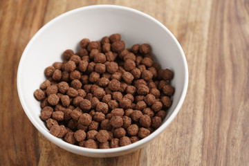 chocolate cereal balls in white bowl for breakfast on wooden table
