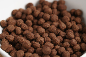 closeup of chocolate cereal balls in white bowl for breakfast on wooden table