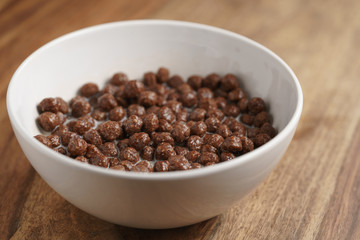 chocolate cereal balls with milk in white bowl for breakfast on wooden table