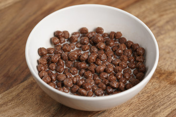 chocolate cereal balls with milk in white bowl for breakfast on wooden table
