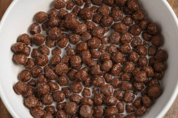 chocolate cereal balls with milk in white bowl for breakfast on wooden table