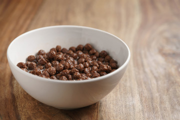 chocolate cereal balls with milk in white bowl for breakfast on wooden table