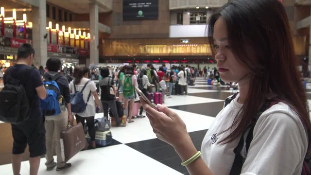 Taipei, Taiwan-29 September, 2015: 4K Asian Woman cheack the phone, crowd of people travelers wait in the line for buy the train ticket in the Taipei main station-Dan