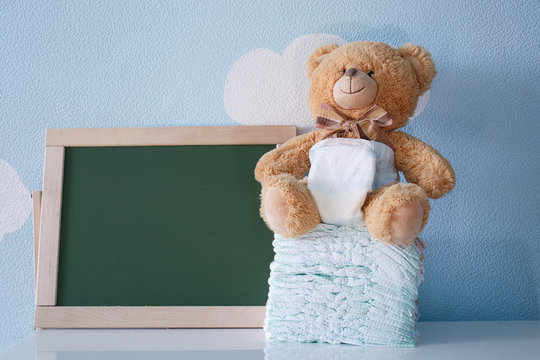 Diapers and blank chalkboard. Teddy bear dressed in diaper. top view. frame with a copy space