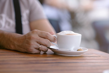Hand of a young man on a wooden table in the cafe with cup of coffee in calm relaxing hand's posture,outdoor blur background